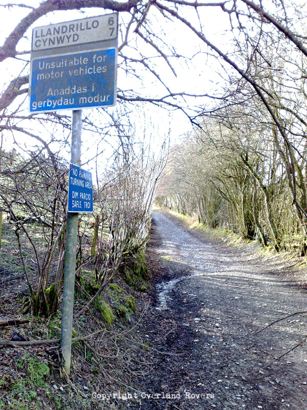 A road sign, at the start of a dirt track, that says "Unsuitable for motor vehicles" and its Welsh translation