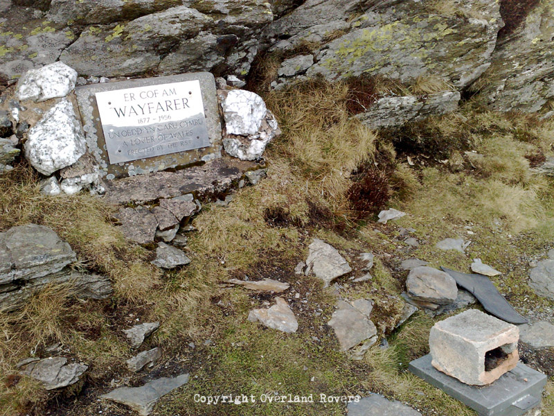 A plaque stuck to stone, commemorating "Wayfarer" found on Wayfarer's Way in Wales. There is a visitor's book, held in a metal box, just visible with a stone on top to keep the lid shut